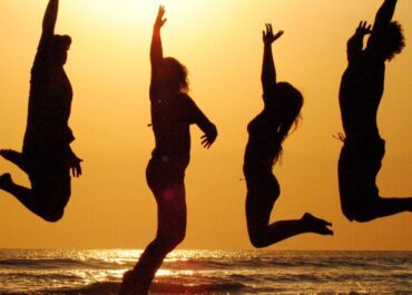 Imagem pessoas felizes pulando a beira mar.